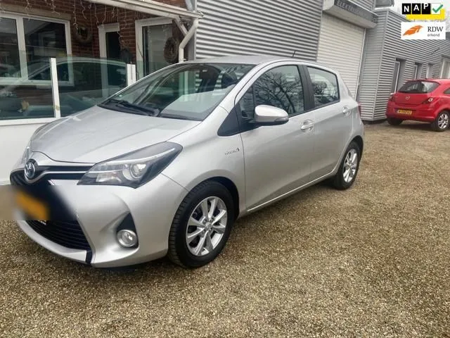 Zilvergrijze Toyota Yaris Hybrid naast de werkplaats van Auto Moos