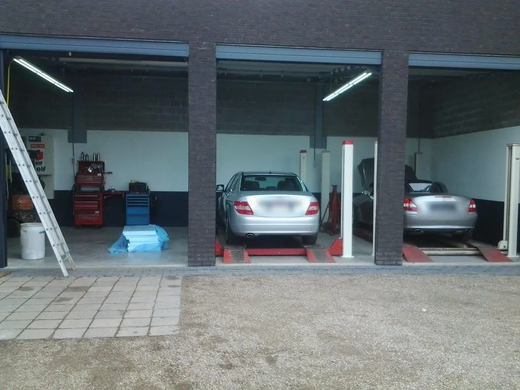 De werkplaats van Auto Moos met open roldeuren, auto's op de hefbrug en gereedschapswagens
