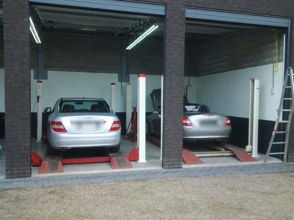 Twee auto's op de hefbruggen in de werkplaats van Auto Moos, gezien door de open roldeuren